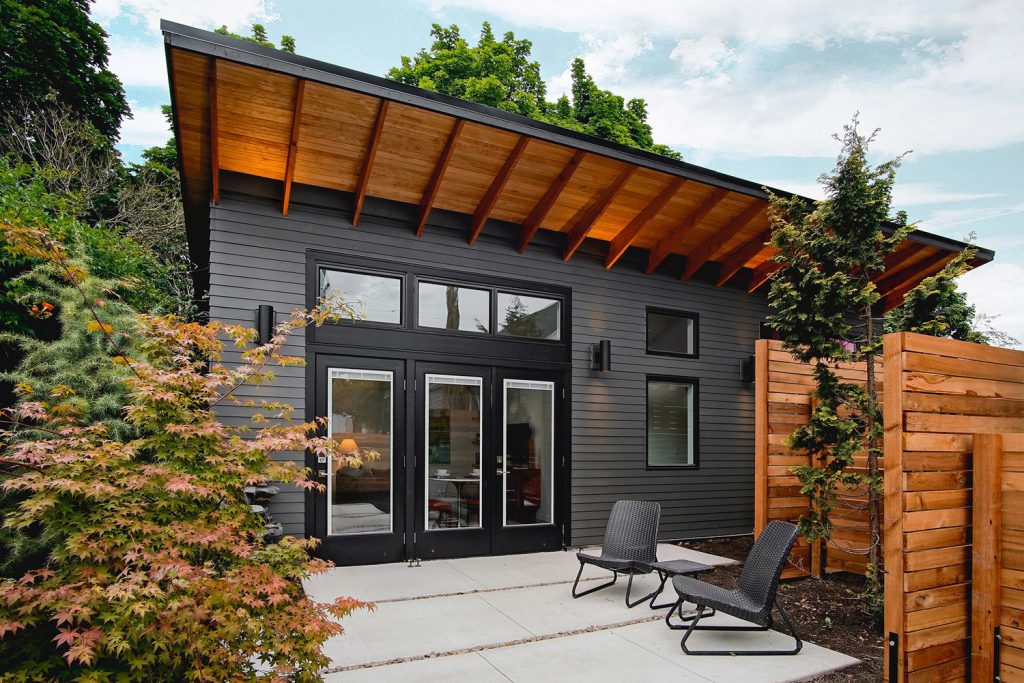 A big ADU House color black with big glass, door with two chairs in the front