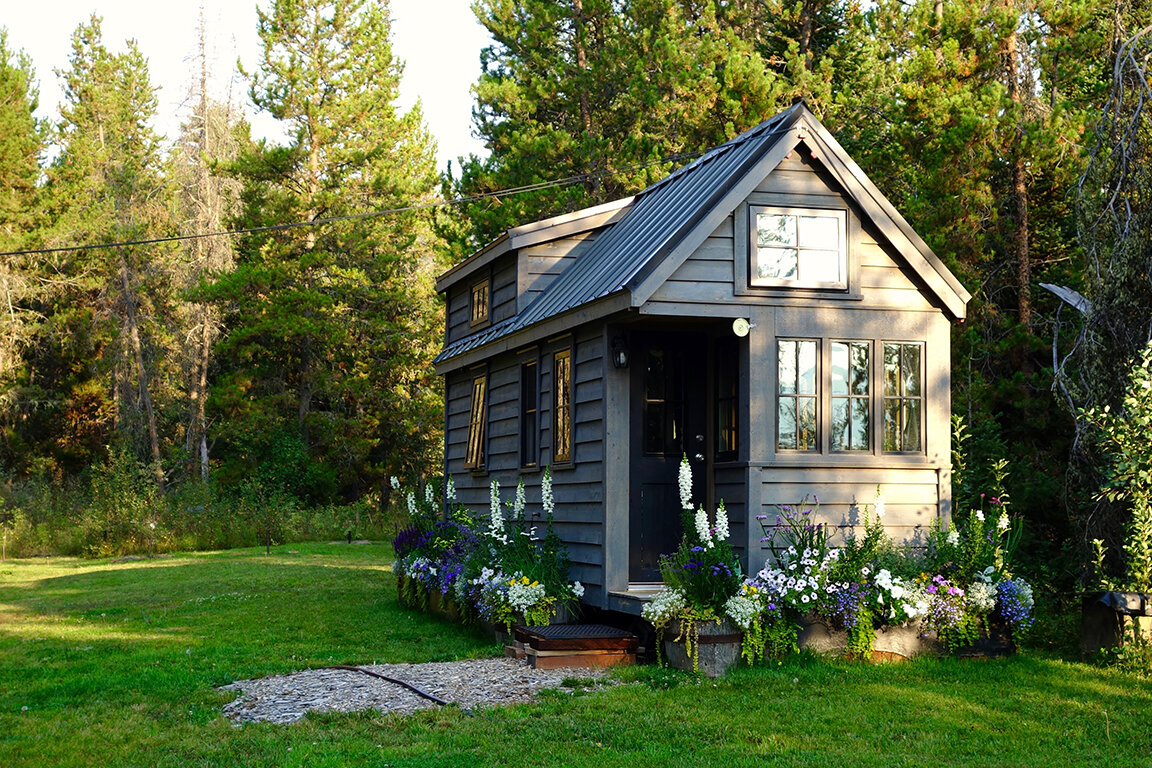 A ADU house in a backyard garden with flowers, big trees and grass