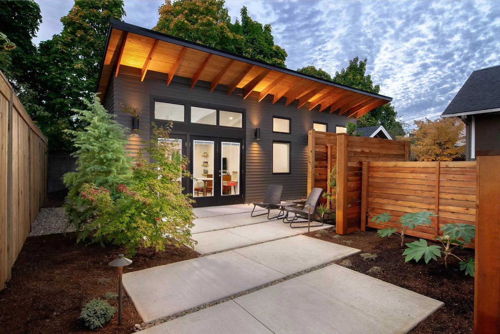 A big ADU House color black with big glass, door with two chairs in the front.